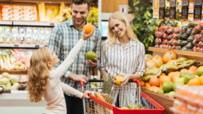 Happy young family standing with a trolley and choosing fruits at the supermarket