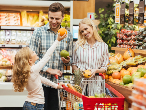 Happy young family standing with a trolley and choosing fruits at the supermarket