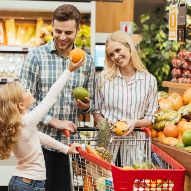 Happy young family standing with a trolley and choosing fruits at the supermarket